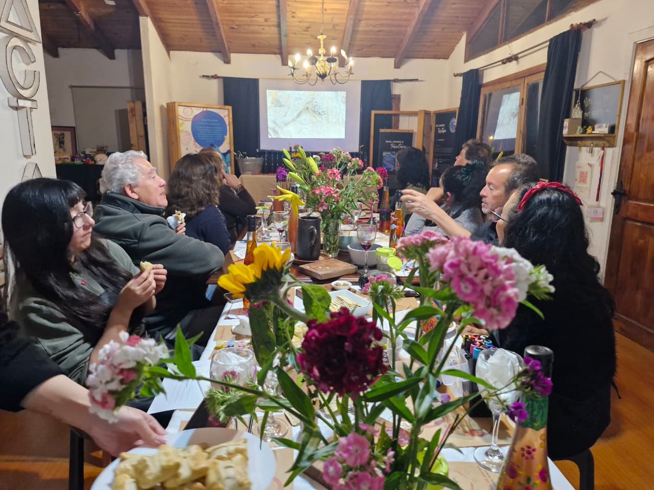 Participantes de una cata de vinos en torno a una mesa con copas, botellas y materiales de pintura
